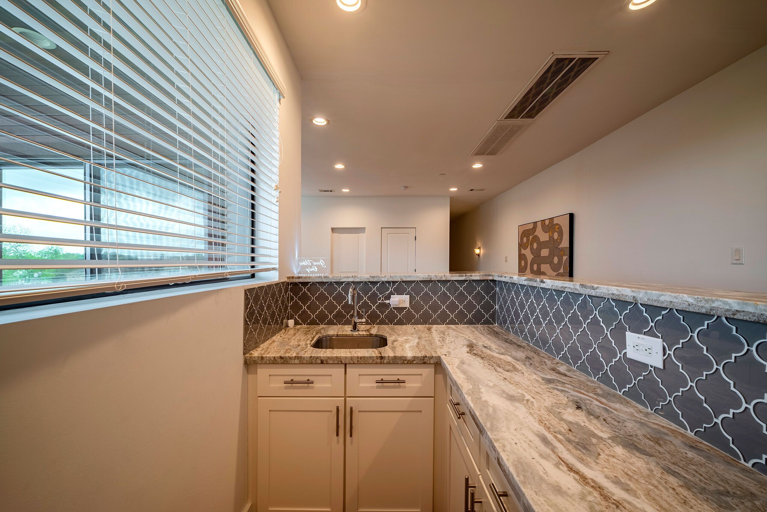 A kitchen with a sink, cabinets, and a patterned backsplash.