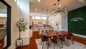 A modern kitchen with white cabinets, a central island with bar stools, and a neon sign on the wall. - Luxury Midtown Houston Home w/ Rooftop Skyline Views (Houston)