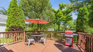 A wooden deck with a table and chairs, a barbecue grill, and a red umbrella.
