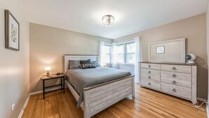 A bedroom with a bed, bedside table, dresser, and a ceiling light fixture.
