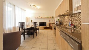 Uma cozinha moderna com armários de madeira, área de jantar com cadeiras, TV e revestimento de azulejos.