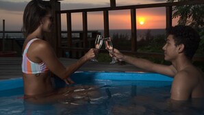 Een koppel proost met champagneglazen in een jacuzzi, met uitzicht op een zonsondergang.