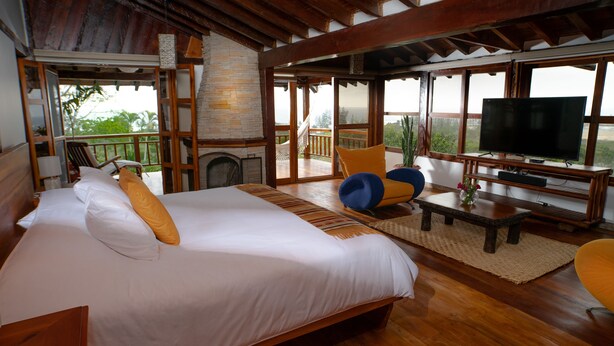 Een ruime kamer met een groot bed, een televisie, een zithoek met een tafel en een balkon met uitzicht.