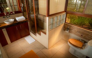 Un baño con tocador de madera, lavamanos blanco, cabina de ducha de vidrio y un inodoro.