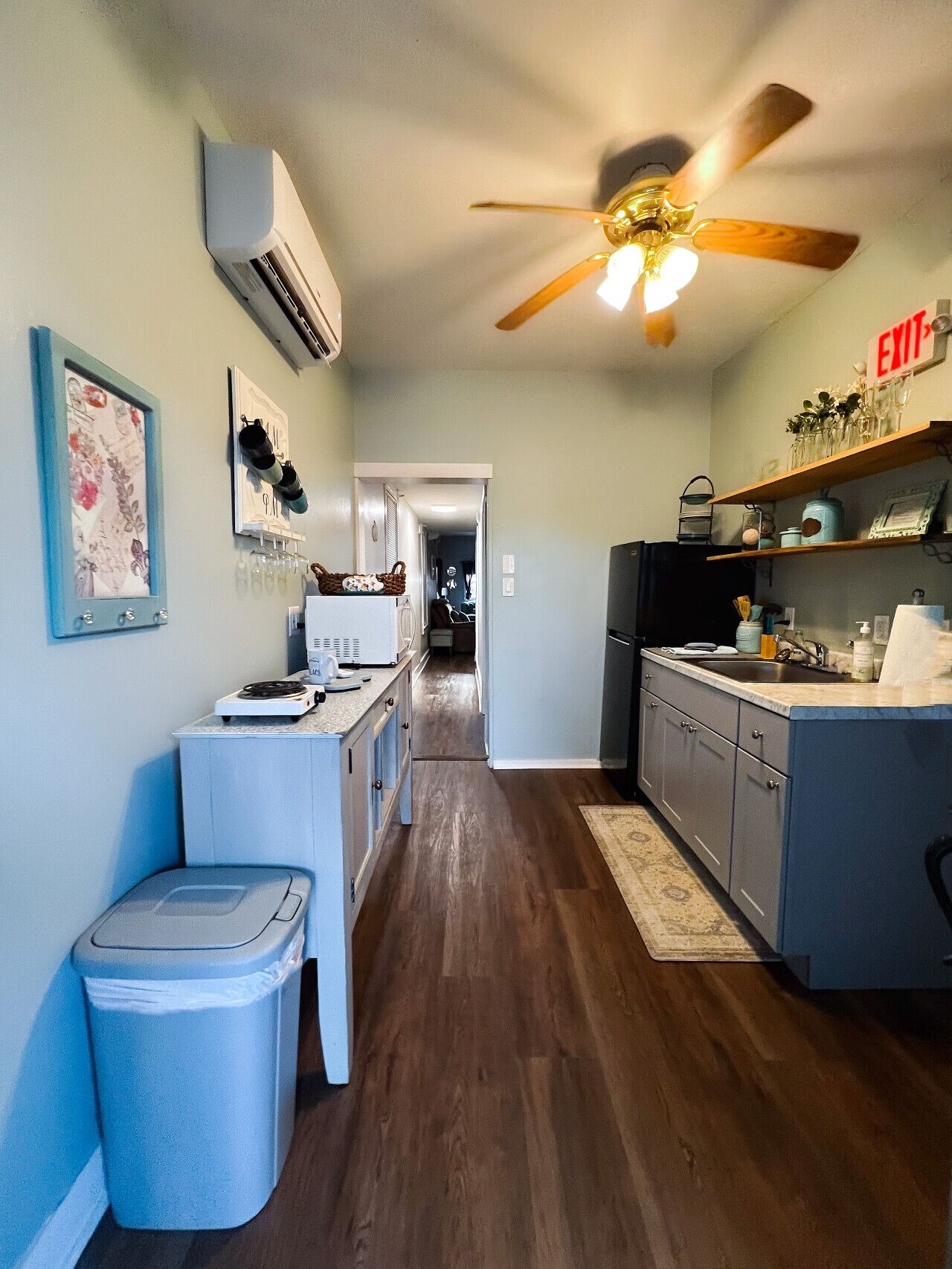 A narrow kitchen with a central island, a ceiling fan, and a trash bin.