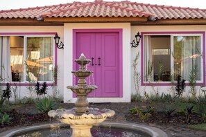 Un bâtiment avec une porte rose, une fontaine et un toit recouvert de tuiles.