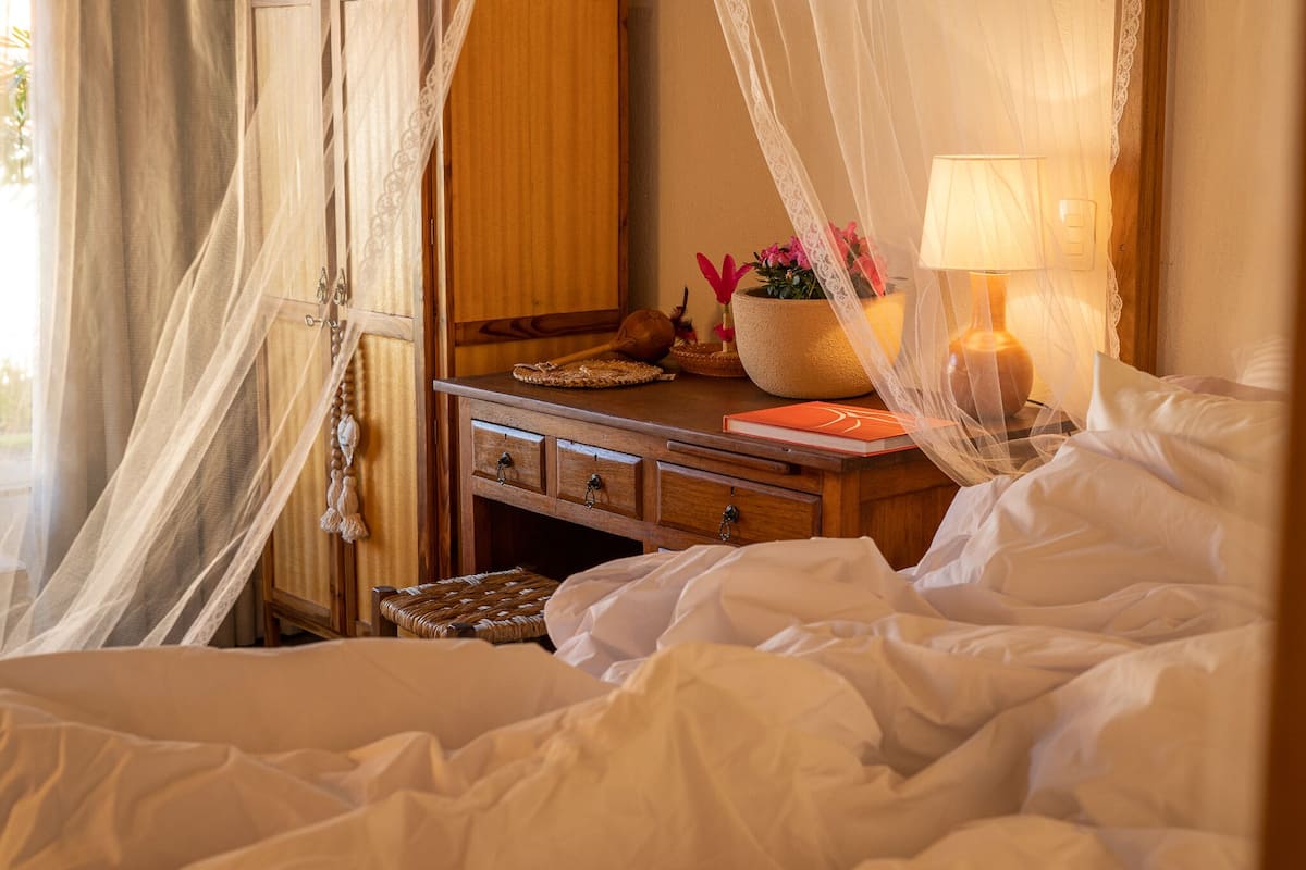 Een net opgemaakt bed met witte lakens, een nachtkastje met een lamp, een kleine decoratieve schaal en een houten nachtkastje.