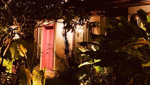 Un bâtiment avec une porte rouge, entouré d’une végétation luxuriante et sous un ciel sombre.