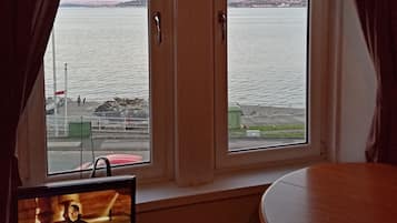 A room with a large window overlooking a body of water, a television on a stand, and a round table.