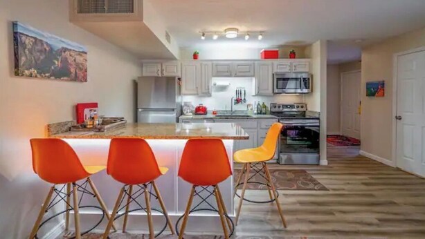 Een moderne keuken met witte kasten, een centraal eiland met oranje barstoelen, roestvrijstalen apparatuur en een rode koelkast.