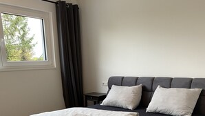 Une chambre moderne avec un grand lit, une tête de lit rembourrée de couleur gris foncé et du linge de lit blanc.