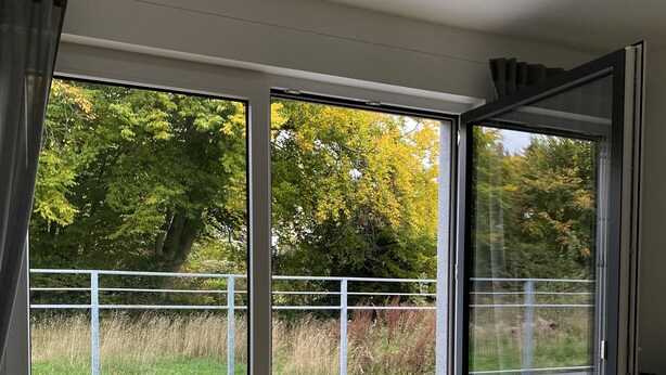 Une chambre moderne dotée d’une grande porte-fenêtre coulissante qui donne sur un espace extérieur offrant une vue sur des arbres et un champ verdoyant.
