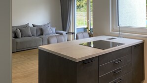 Une cuisine moderne avec un îlot central, un canapé gris et une grande fenêtre qui laisse entrer la lumière naturelle.
