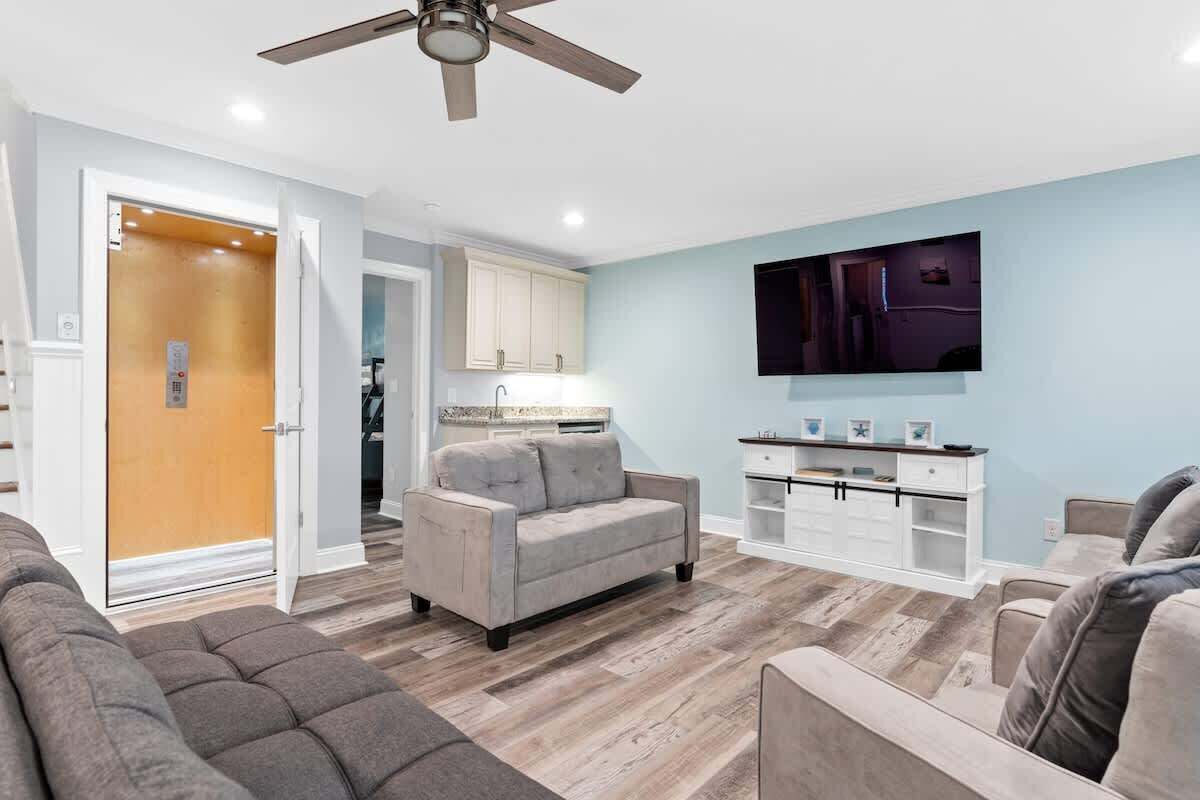 A living room with a sofa, a TV mounted on the wall, and a kitchen area with cabinets and a countertop.