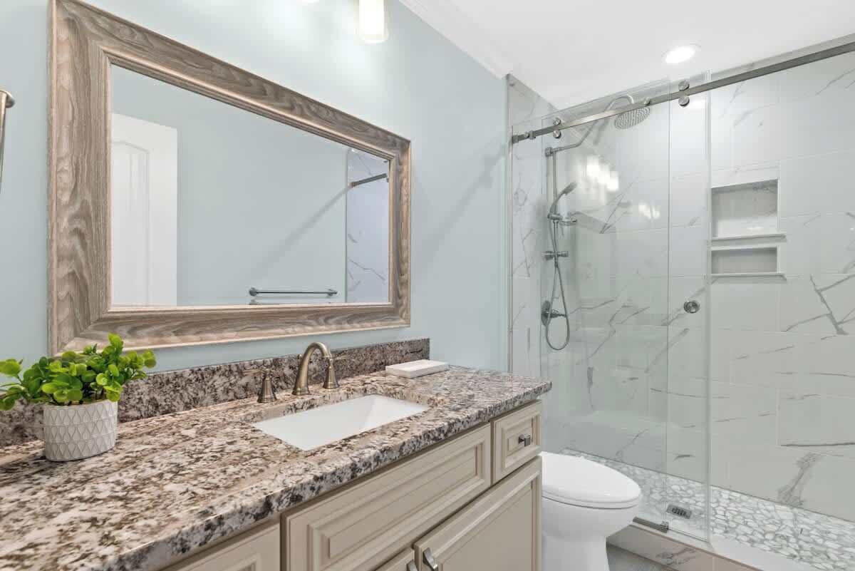 A bathroom with a marble countertop, a sink, a toilet, and a glass shower enclosure.