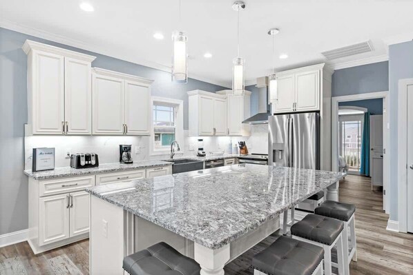 A modern kitchen with white cabinets, a granite island, and stainless steel appliances. - East End Views (Ocean Isle Beach)