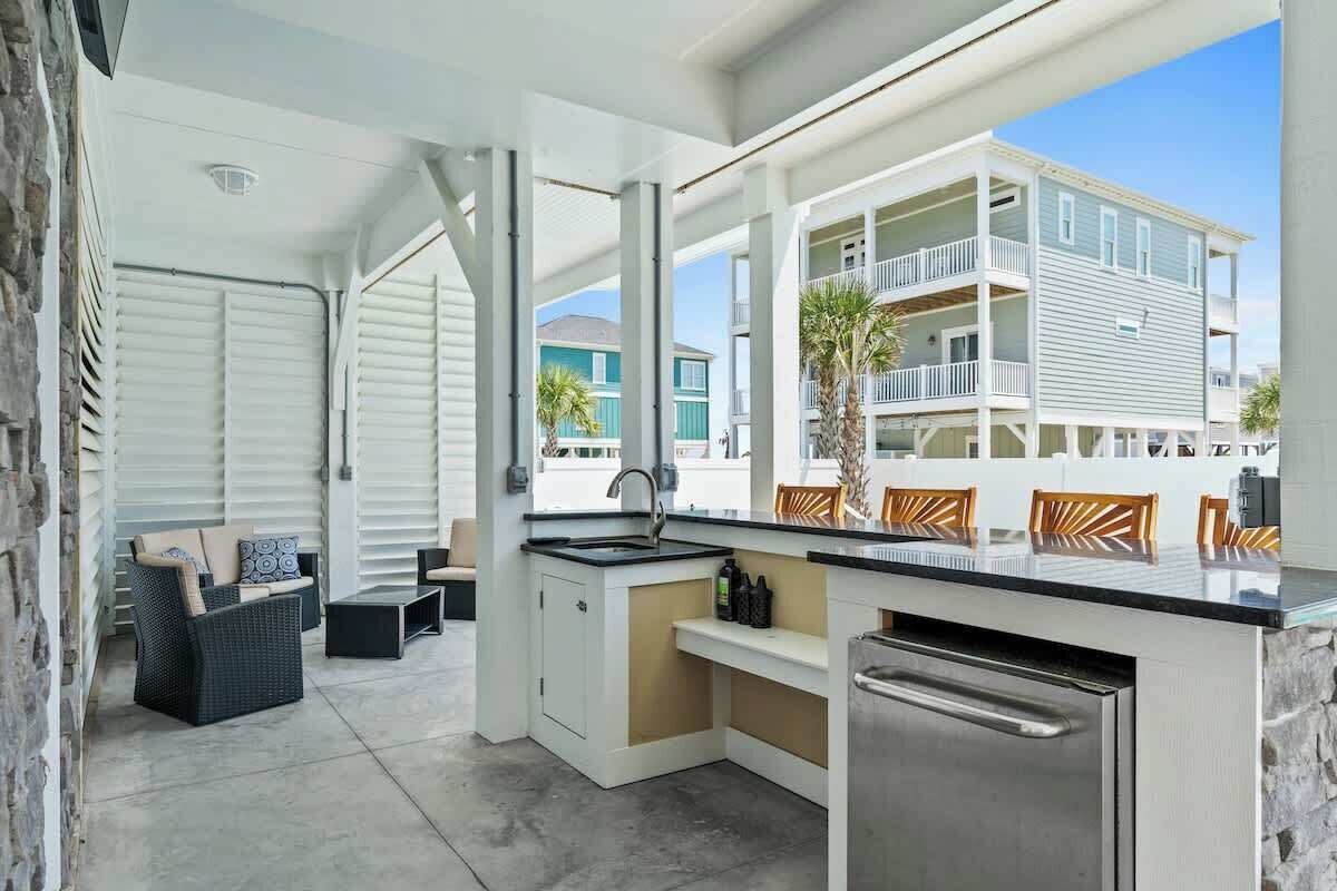 A covered outdoor kitchen with a sink, a dining area with chairs, and a view of a building with balconies.