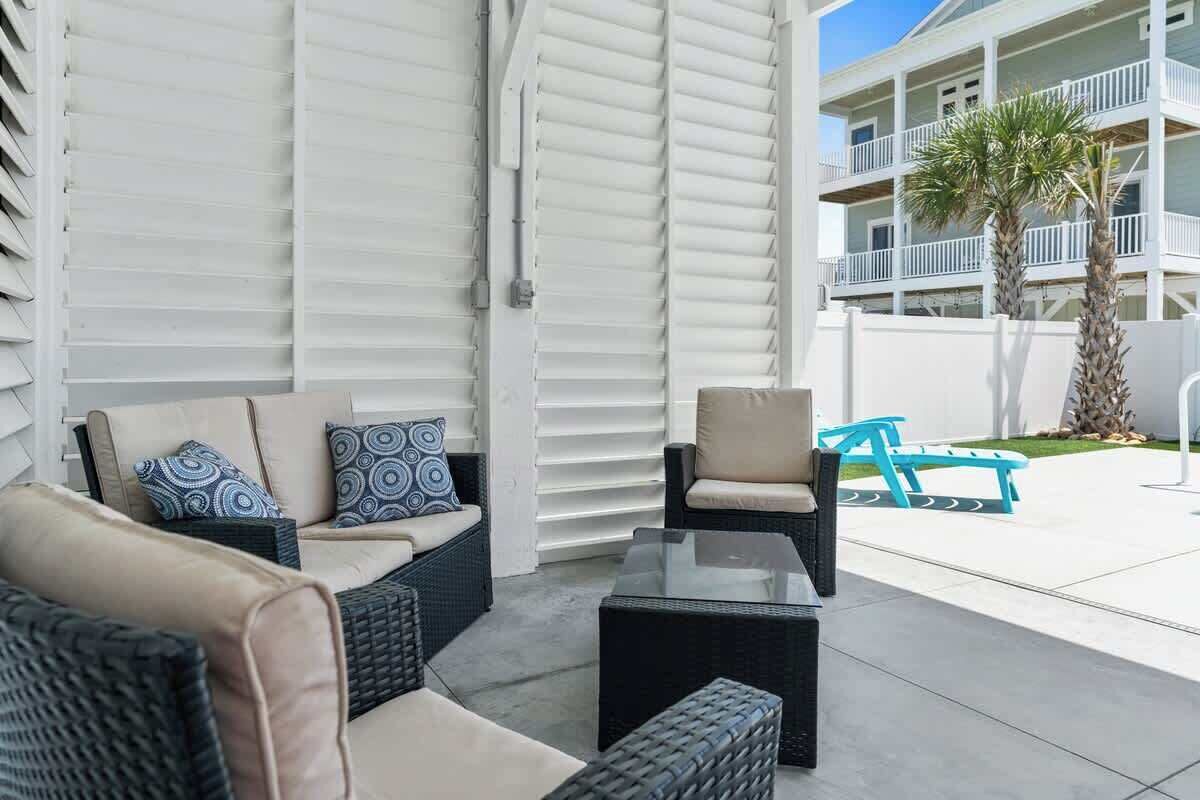 A covered outdoor seating area with wicker furniture, a glass-top coffee table, and a blue bench.