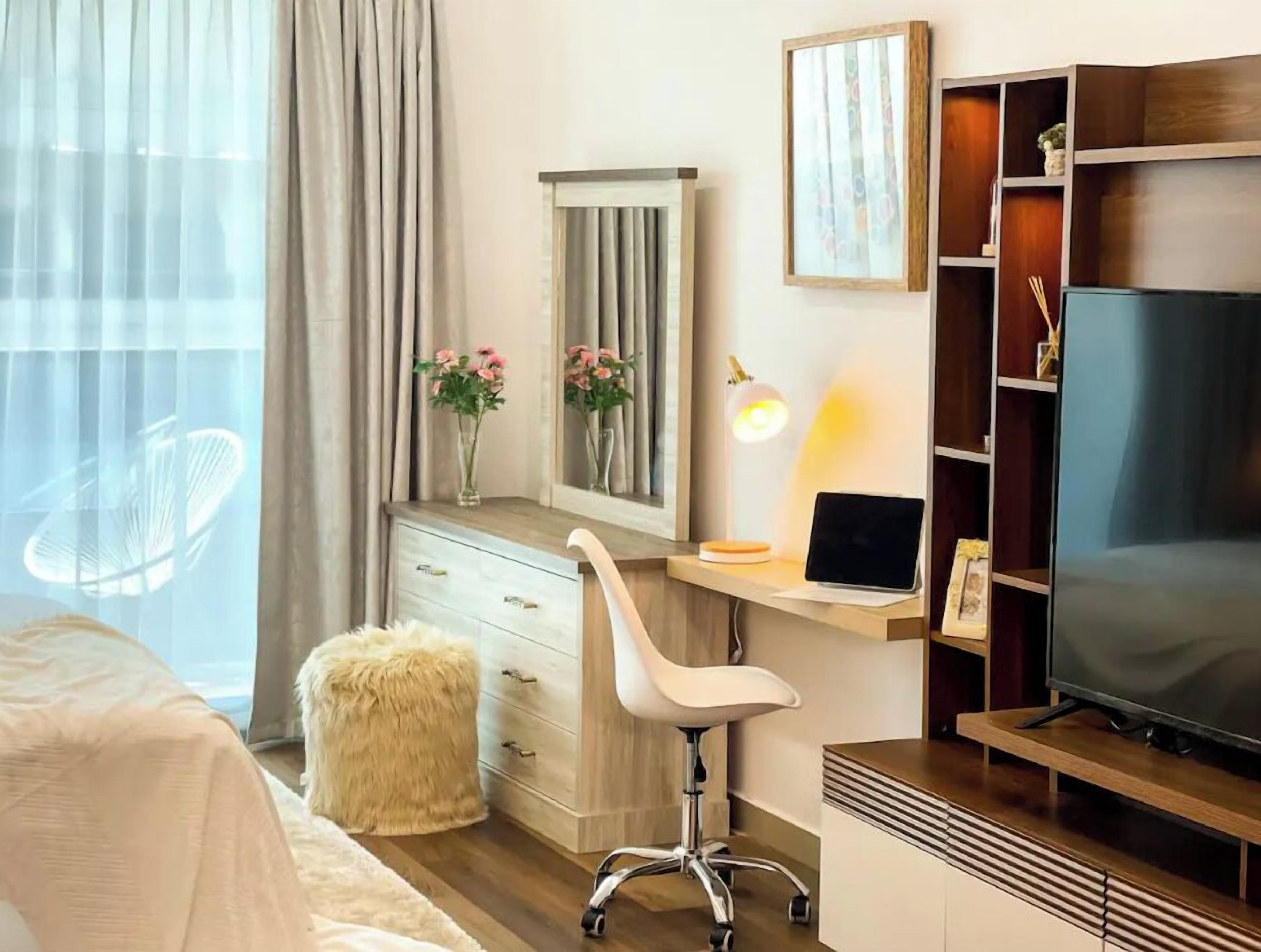 Une chambre d’hôtel avec un lit, un bureau avec un ordinateur portable, une télévision, un miroir et une petite plante.