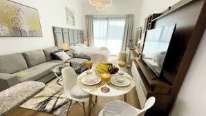 Uma sala de estar moderna com área de jantar, um sofá cinza, uma televisão e uma mesa de jantar posta com pratos, copos e frutas.