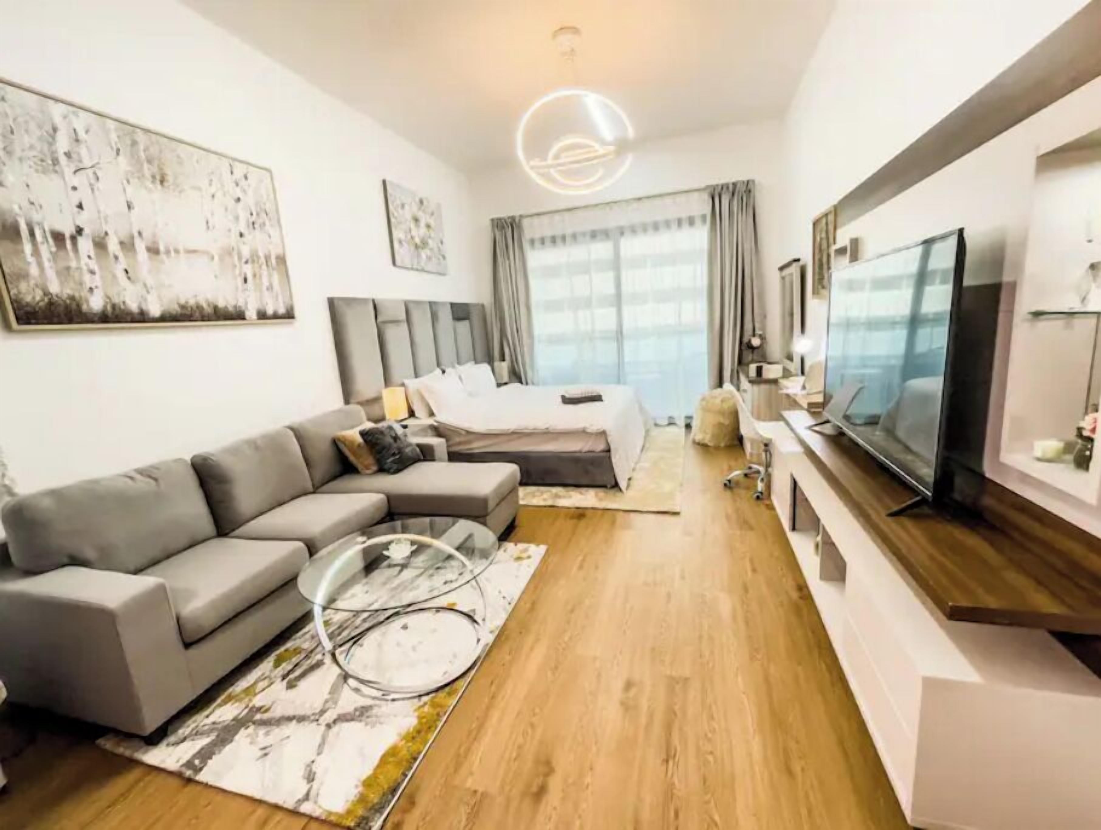 Habitación de hotel moderna con una cama grande, un sofá gris, un televisor y un cuadro en la pared.
