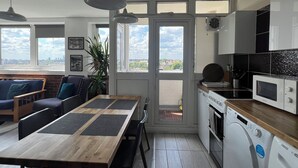 A modern kitchen with a wooden table, built-in appliances, and large windows offering a city view. - Fantastic View over London apartment in Abbey Road (London)