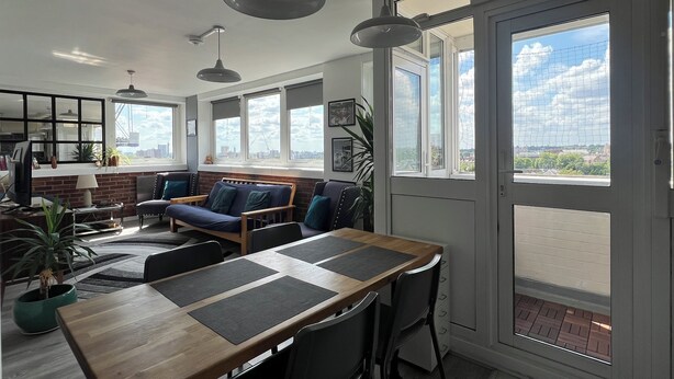 A modern living room with a wooden dining table, comfortable seating, large windows, and a city view. - Fantastic View over London apartment in Abbey Road (London)