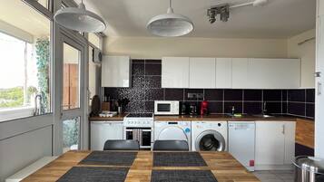 A modern kitchen with a wooden dining table, built-in appliances, and a view of the outdoors.