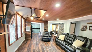 Un vaste espace de vie doté d’un plancher en bois, d’un canapé en cuir, d’un téléviseur fixé au mur et d’un ventilateur de plafond.