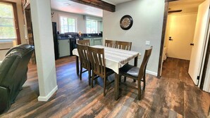 Un coin repas avec une table et des chaises en bois, une cuisine à l’arrière-plan et une horloge au mur.