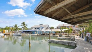 Une zone riveraine avec un quai en bois, un bateau et un bâtiment portant l’inscription « BUREAU DU PORT D’ABRI ANTI-OURAGAN ».