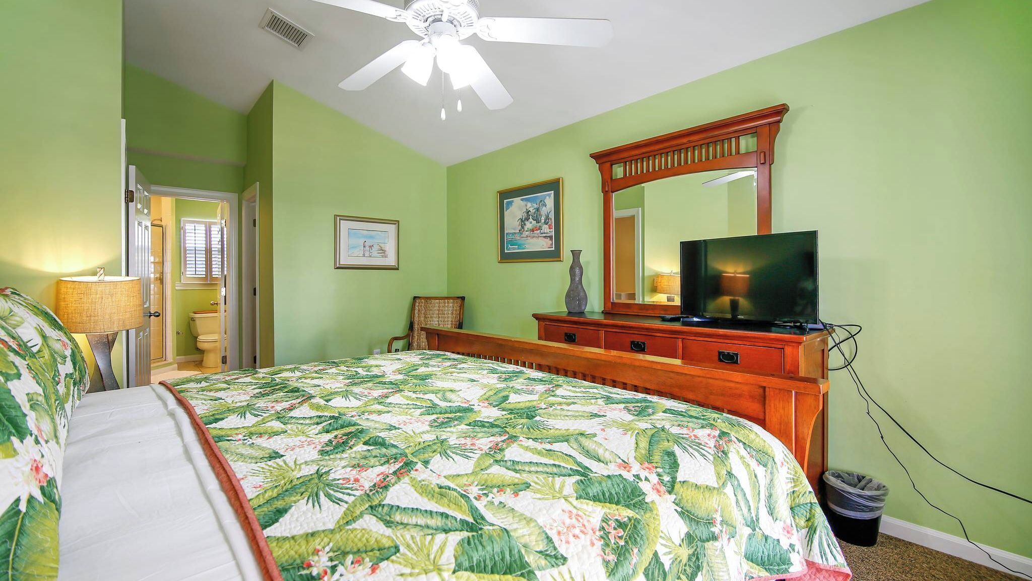 A bedroom with a bed, a dresser, a television, and a ceiling fan.