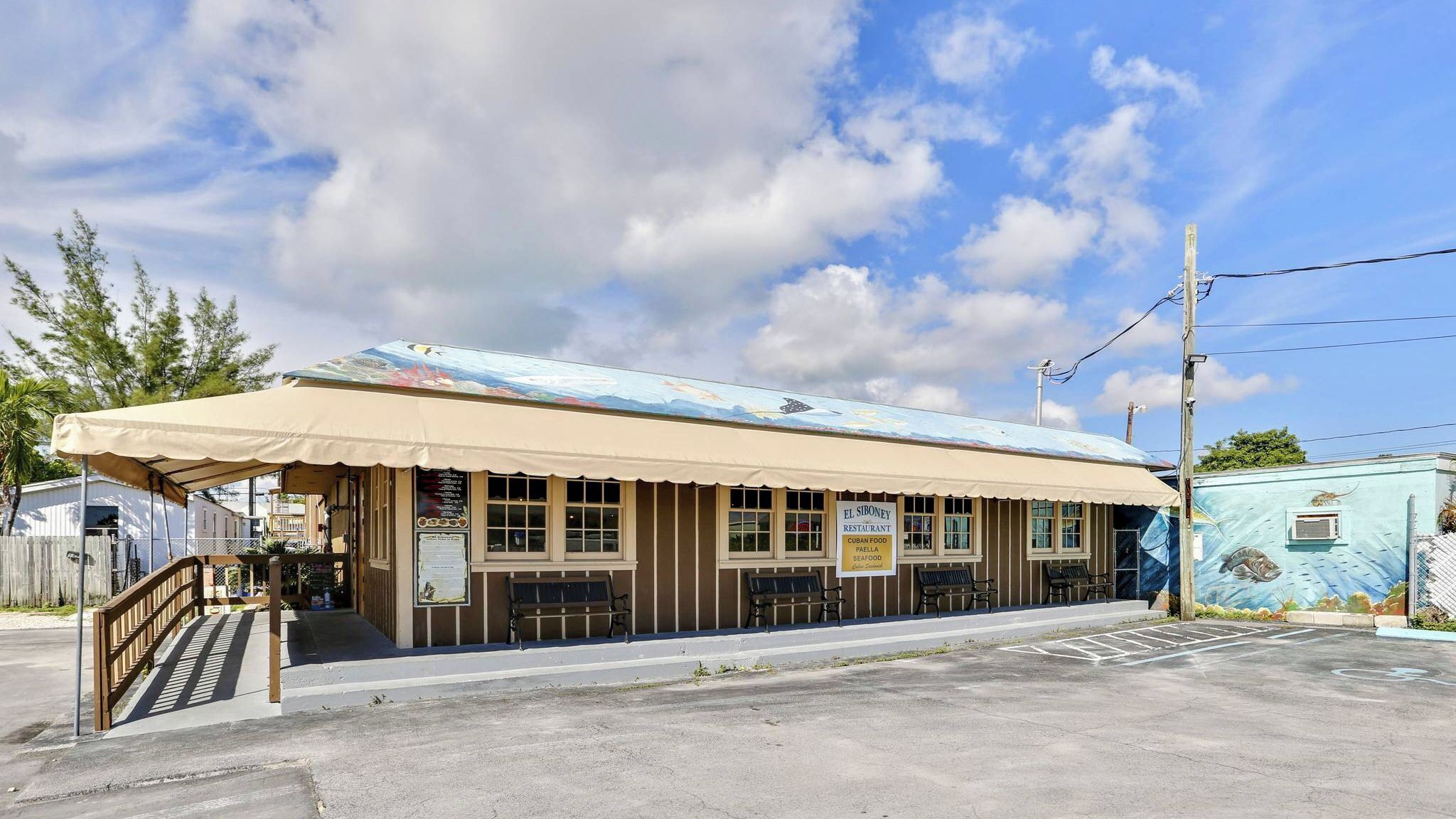 A small building with a covered outdoor seating area, a signboard, and a mural on the side.