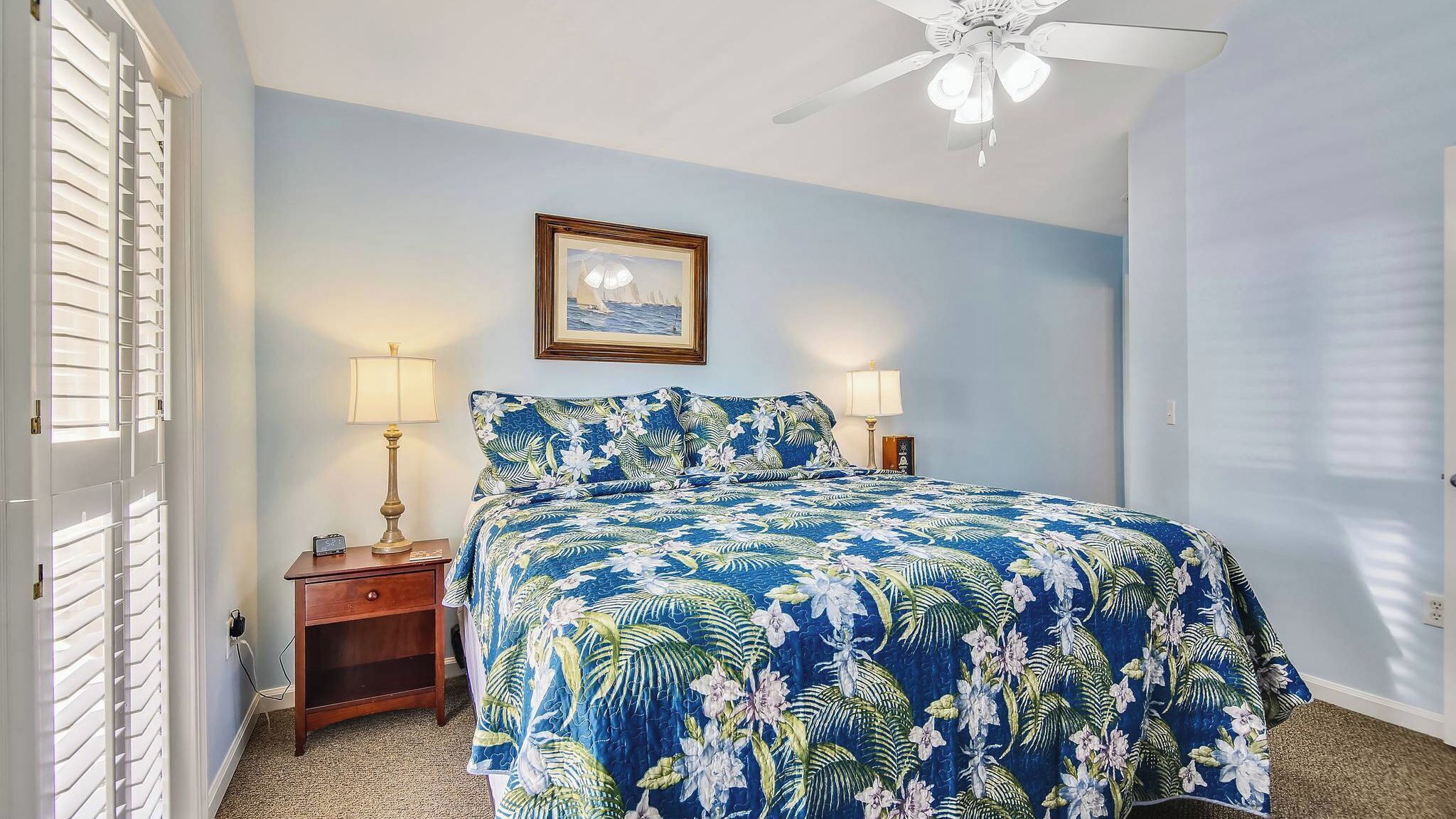 A bedroom with a bed, two bedside tables, a ceiling fan, and a framed picture on the wall.