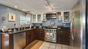 A kitchen with wooden cabinets, a stainless steel refrigerator, a stove, and a microwave. - La Casita by Avantstay Steps to Duval Street in Key West! Month Long Stays Only (Key West)