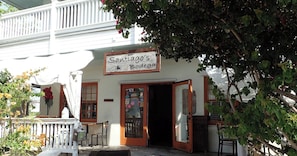 A building with a sign reading 'Santiago's Bodega,' a wooden door, and a white porch with a chair. - La Casita by Avantstay Steps to Duval Street in Key West! Month Long Stays Only (Key West)