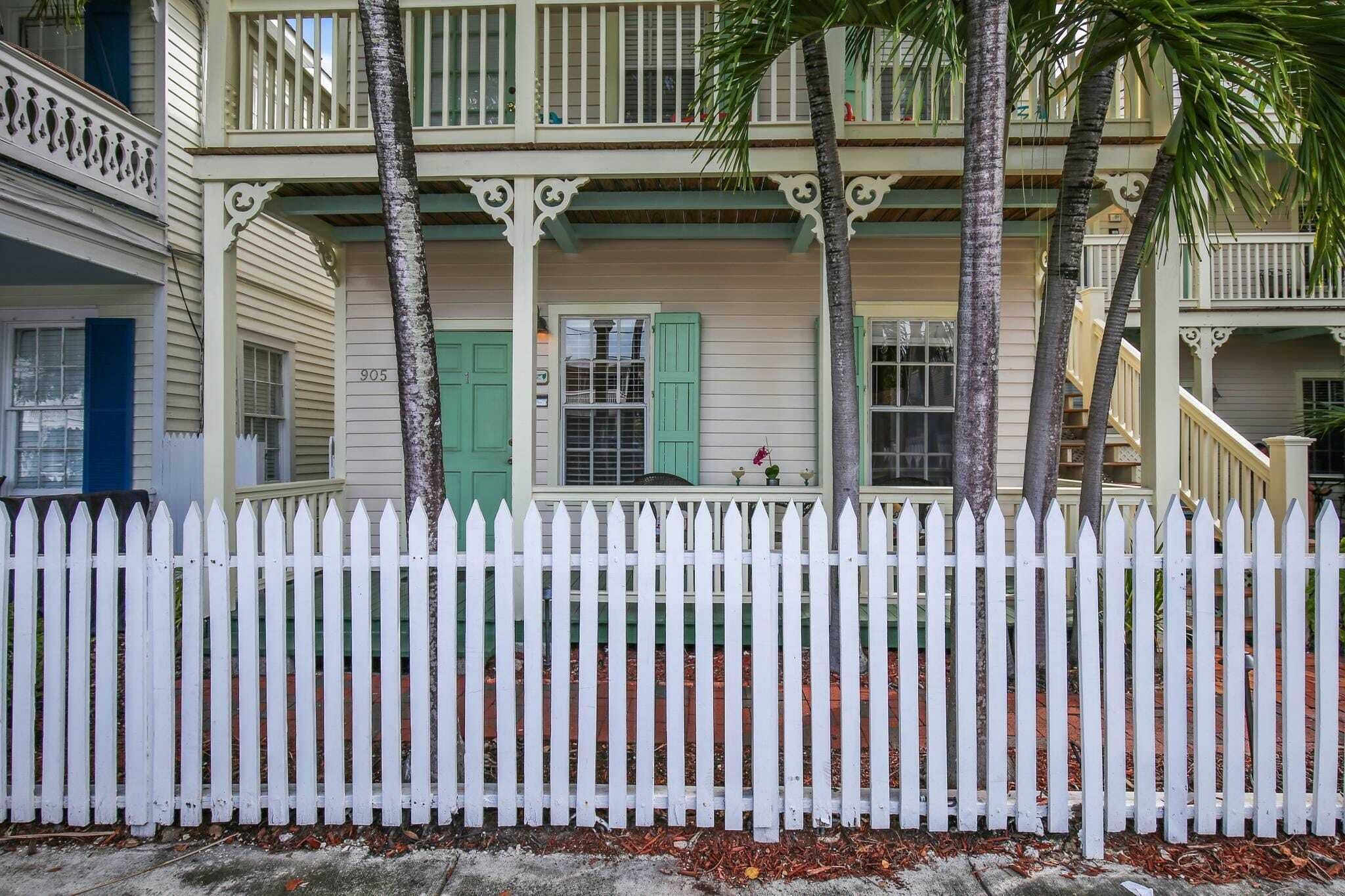 A two-story building with a white picket fence, green shutters, and a balcony with a railing.