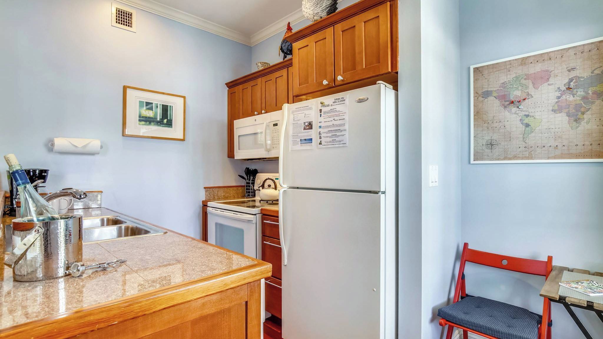 Une cuisine compacte avec des meubles en bois, un réfrigérateur blanc, un four à micro-ondes, un évier et un petit coin repas avec une chaise.