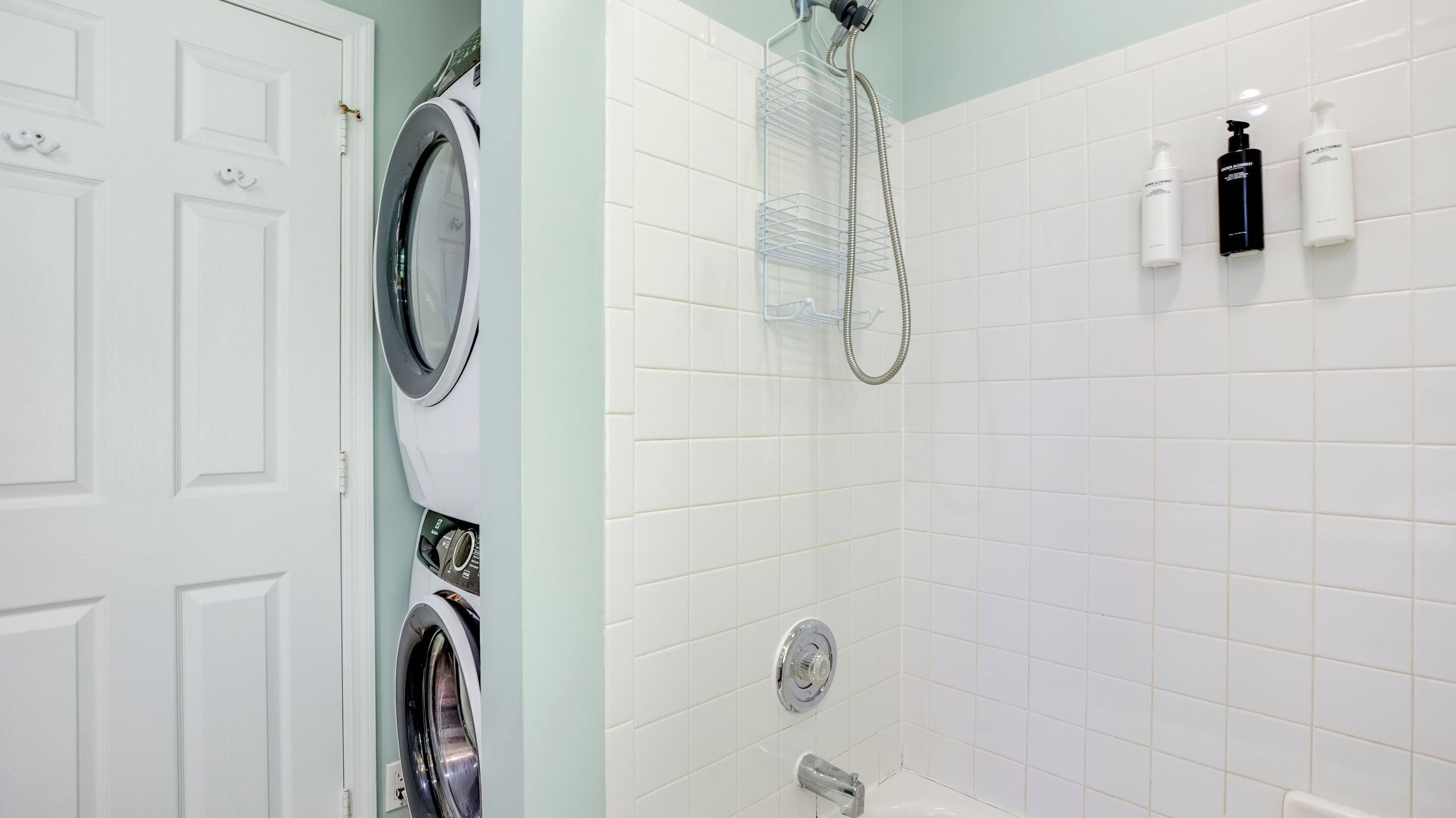 Un baño con lavadora, ducha y artículos de aseo en la pared.