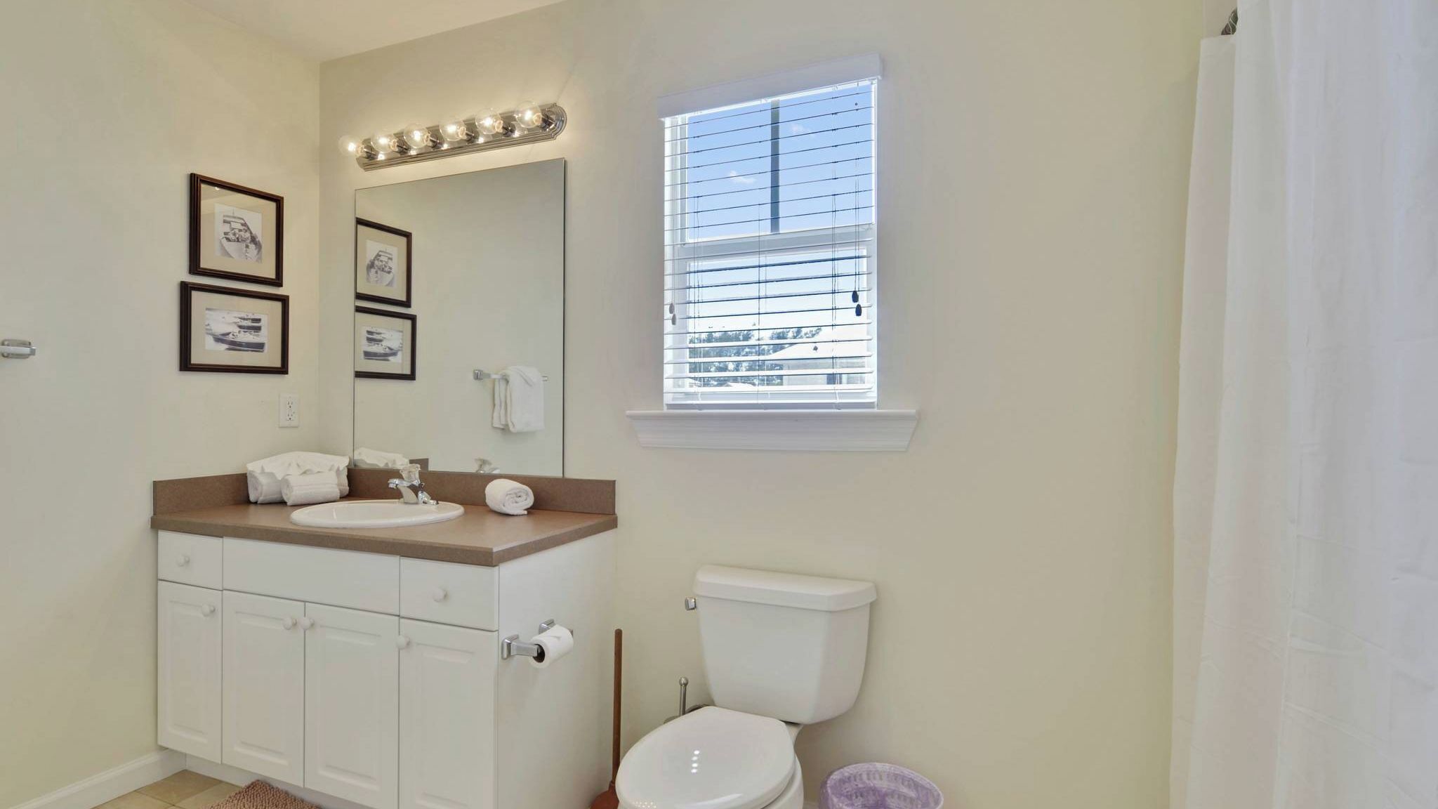 A bathroom with a sink, mirror, toilet, and window with blinds.