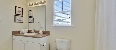 A bathroom with a sink, mirror, toilet, and window with blinds.