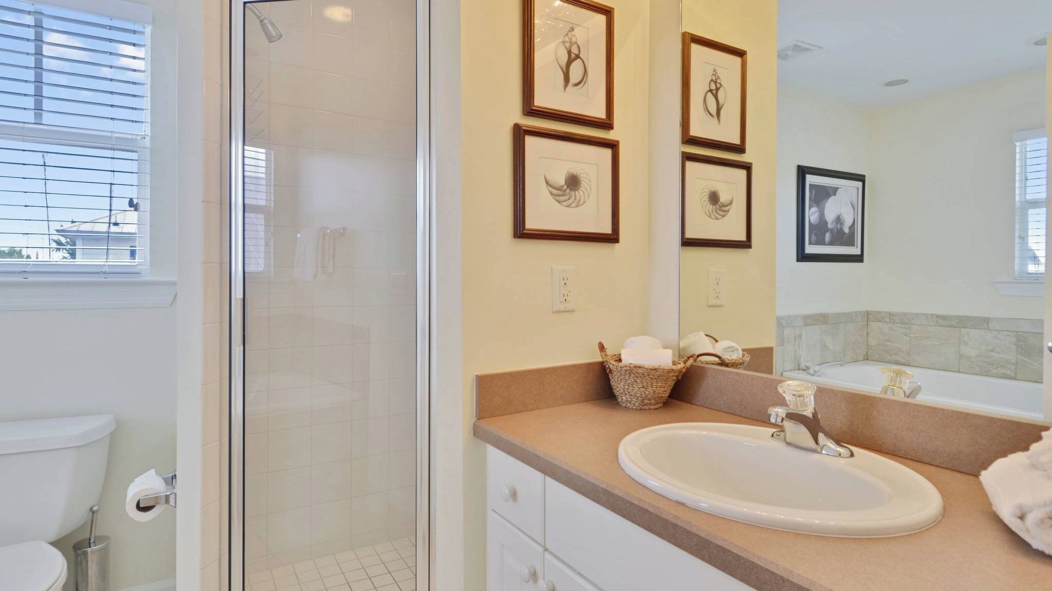 A bathroom with a glass shower enclosure, a sink with a mirror, and framed artwork on the wall.