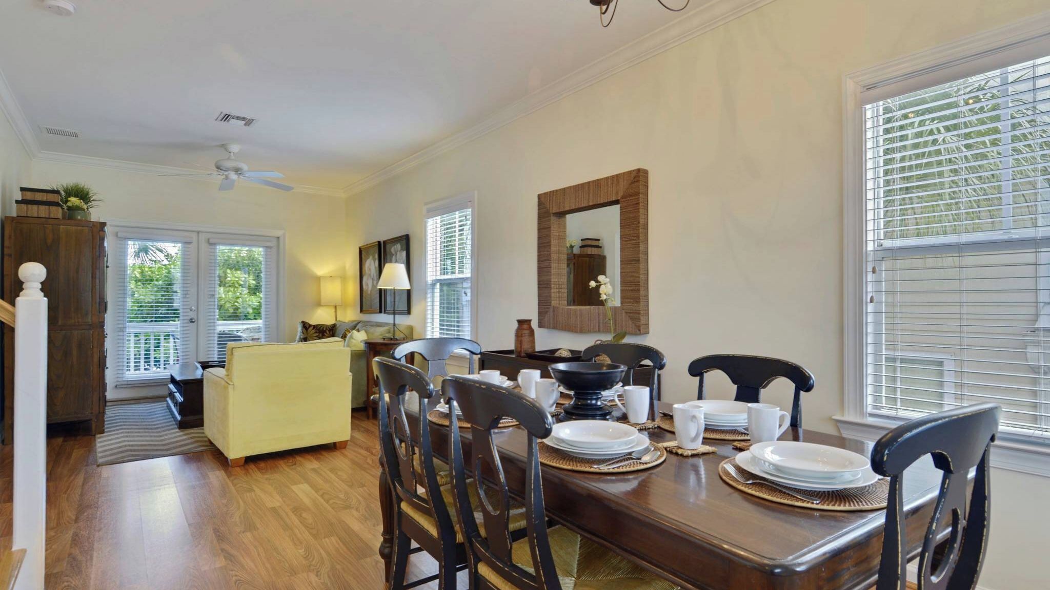 Un coin repas avec une table en bois dressée pour quatre personnes, un canapé et une fenêtre avec des stores.