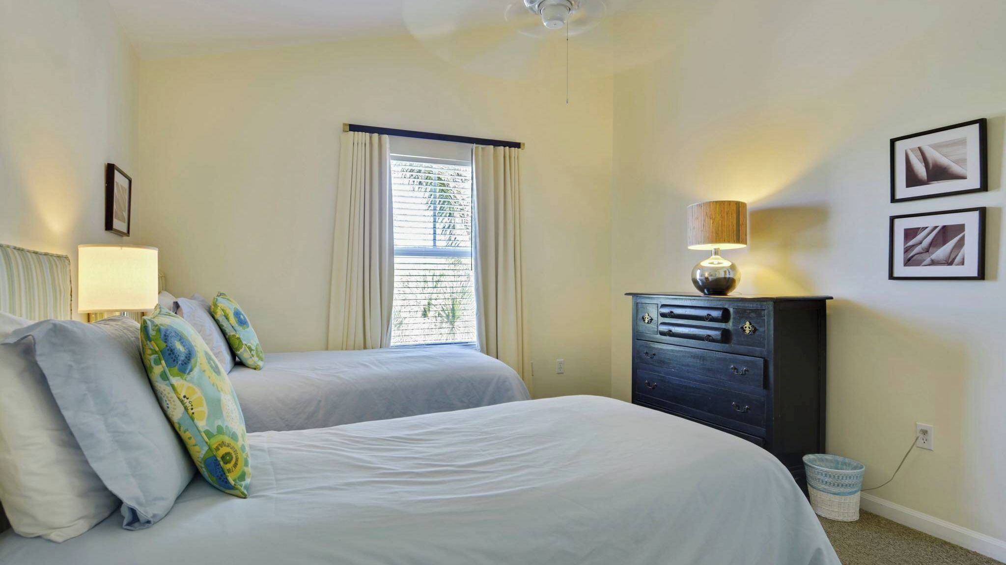 A bedroom with two beds, a dresser, a lamp, and a window with curtains.