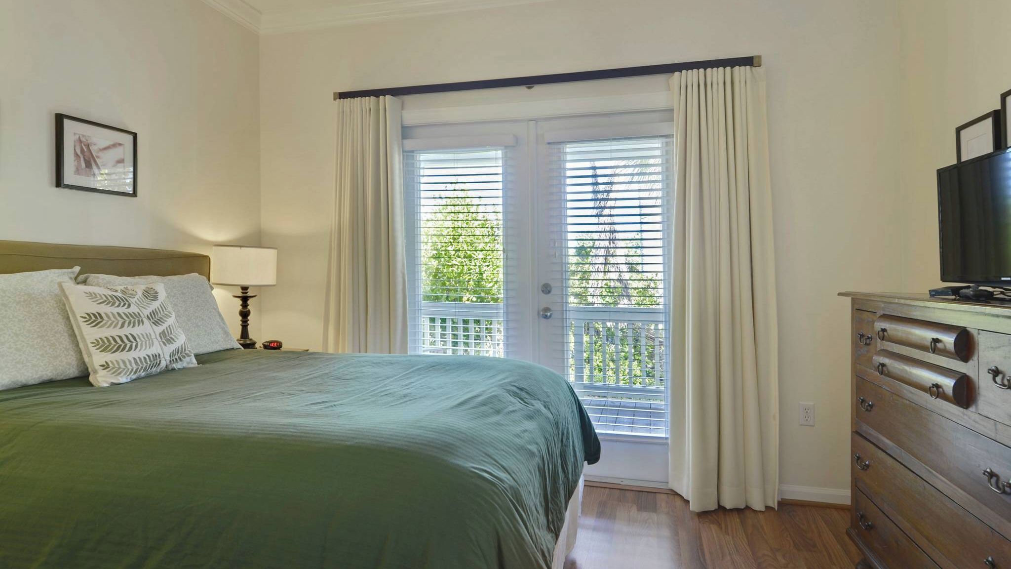 Een slaapkamer met een bed, een dressoir, een televisie en een raam met gordijnen.