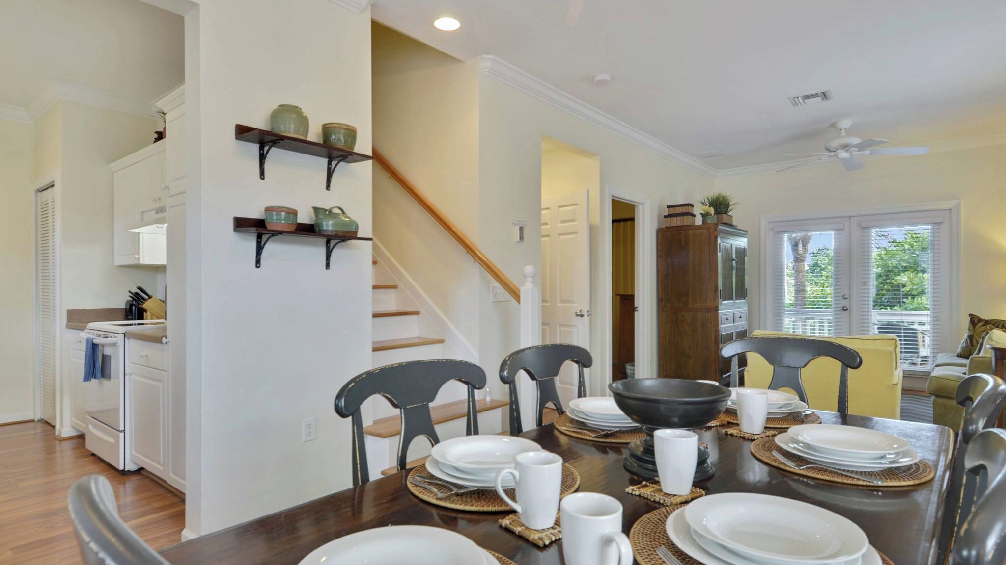 A dining area with a wooden table set for four, chairs, and a staircase leading to another level.
