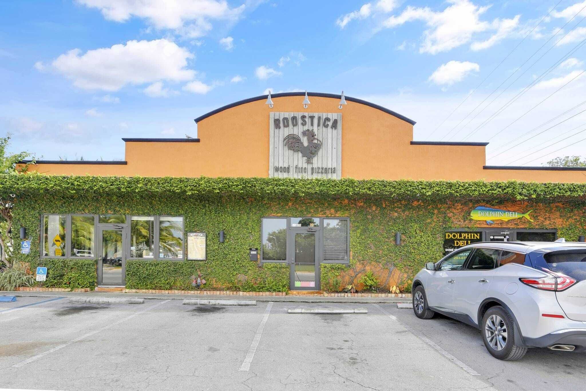 Un edificio con un letrero que dice "Roostica Wood Fired Pizzeria" y un letrero que dice "Dolphin Deli".