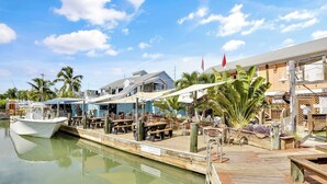 Un restaurant situé au bord de l’eau, doté d’une terrasse, avec un bateau amarré et un bâtiment sur lequel on peut lire l’inscription « EXISTENCE ».