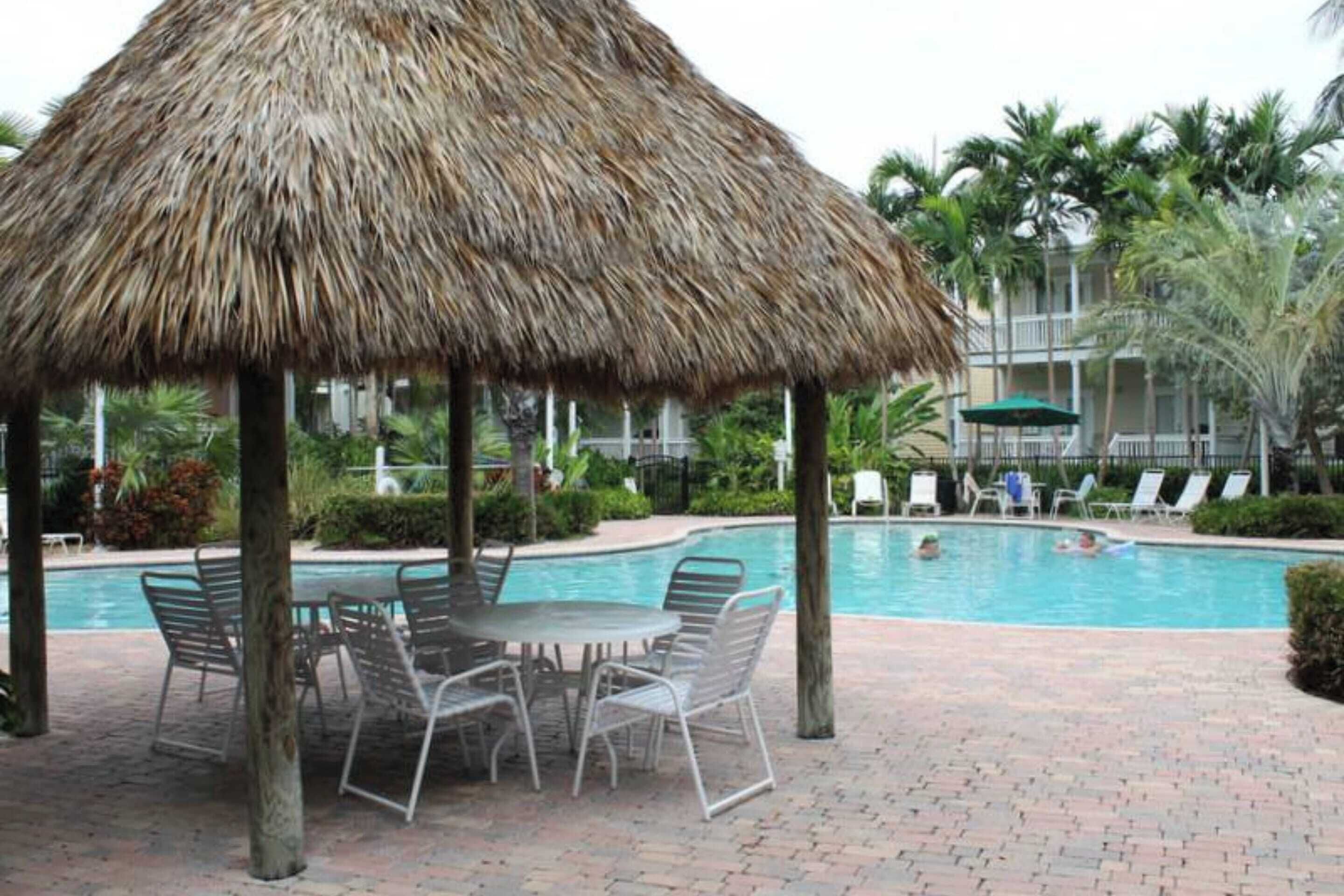 Un espace aménagé au bord de la piscine, avec un parasol en chaume, des chaises longues et une piscine.