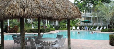 Un espace aménagé au bord de la piscine, avec un parasol en chaume, des chaises longues et une piscine.